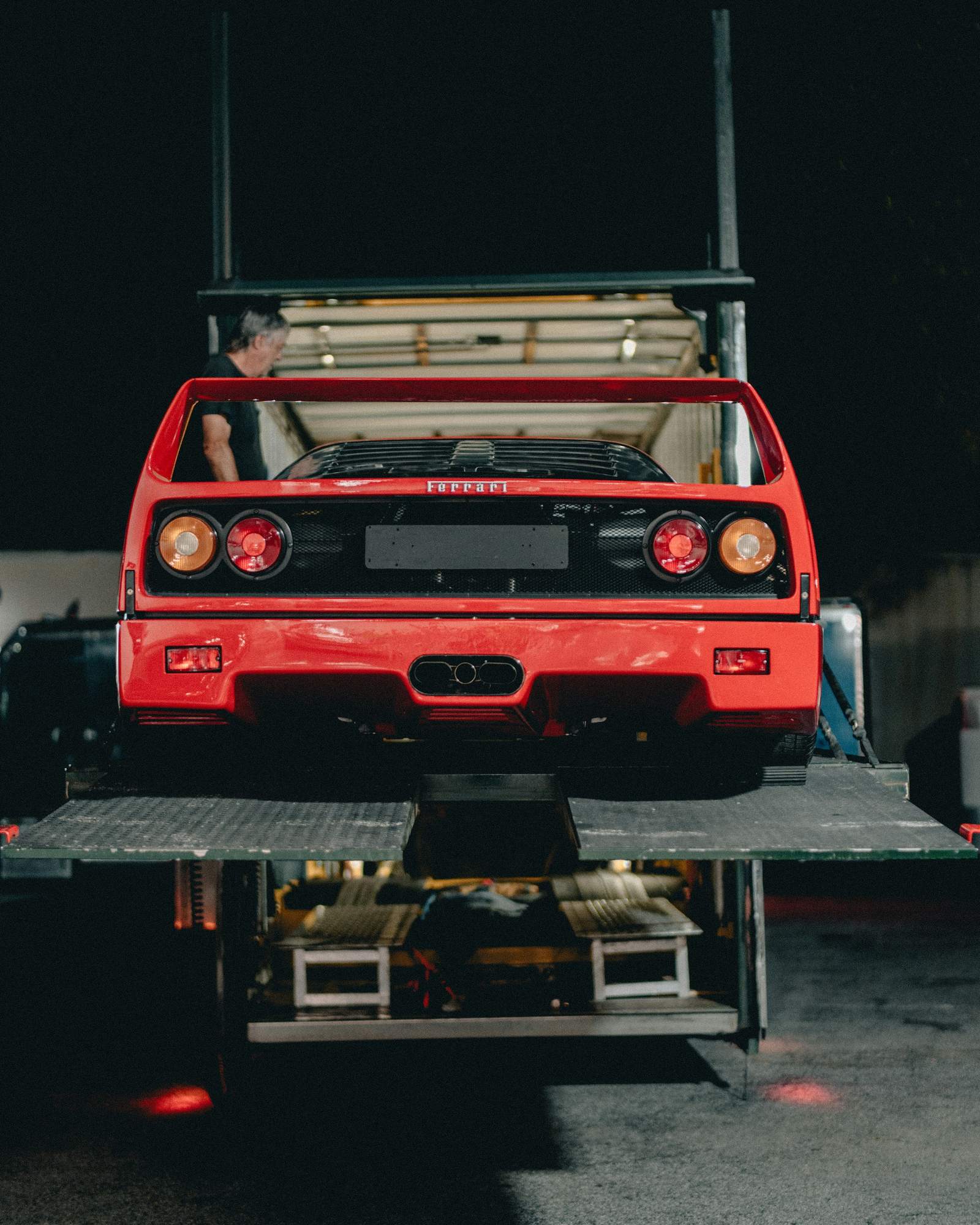 A red Ferrari F40 on the tail-lift of an enclosed car transporter at night