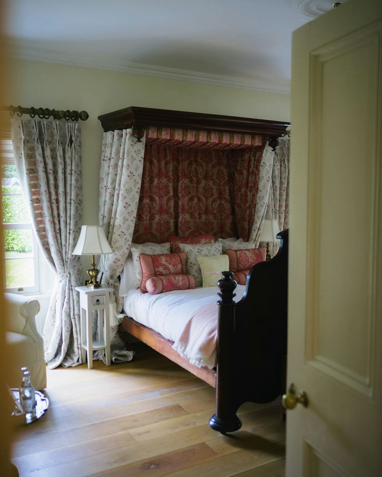 A country-house bedroom with a canopied bed, seen through a panelled door