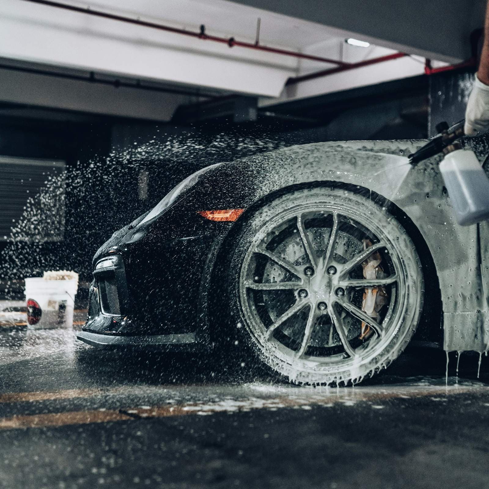 A black sports car being sprayed with snow foam in a garage